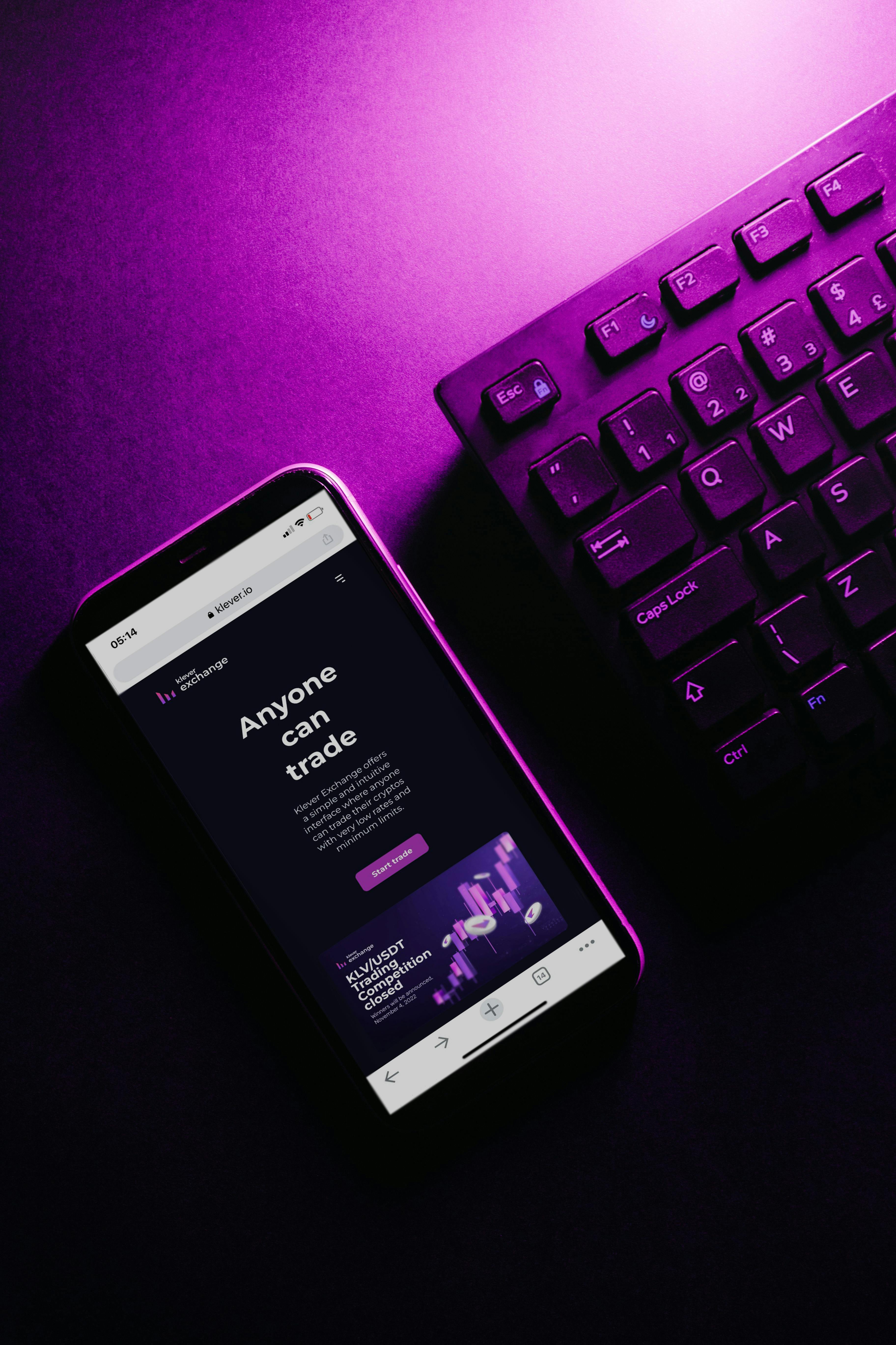 Close-up of a smartphone and keyboard under vibrant purple lighting, showcasing modern tech aesthetics.
