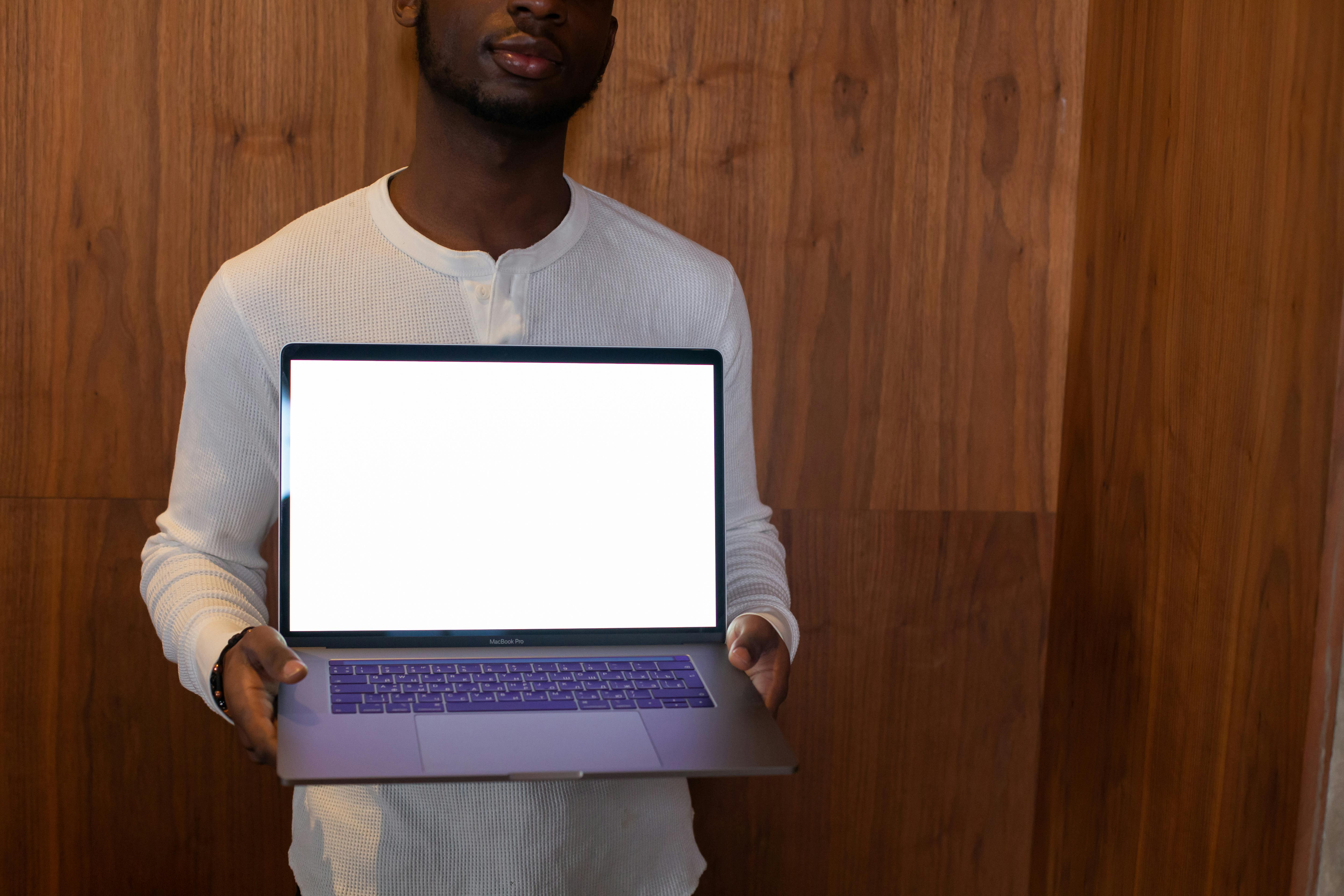 A man holding a laptop with a blank screen, standing indoors against a wooden background.